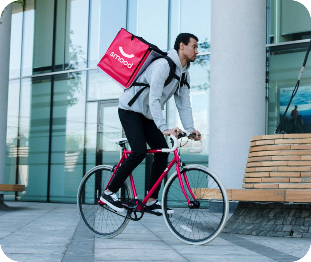 Smood food delivery man on a bicycle in a city street, carrying an insulated rucksack.